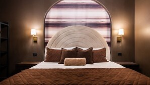 Un dormitorio con una cama grande, un cabecero de diseño curvo, dos lámparas de noche y vistas a través de una ventana con un diseño a rayas.