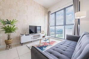 A modern living room with a large window, a grey sofa, a television on a white cabinet, and a potted plant. - Cozy Oasis near Ikea TRX Mall King Size Bed 100mb (Kuala Lumpur)