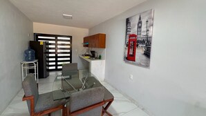 A dining area with a glass table and chairs, a water dispenser, a refrigerator, and a wall-mounted telephone booth artwork.