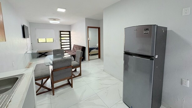A compact kitchen with a refrigerator, a dining table with chairs, and a small sink.