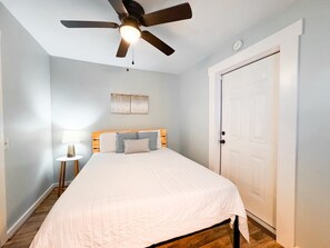 A bedroom with a bed, a ceiling fan, a nightstand, a lamp, and a door.