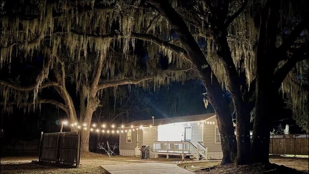 A house with a porch, string lights, and large trees. - Cozy Beaufort Cottage - Near Parris Island & Downtown (Beaufort)