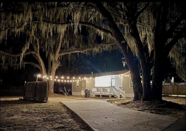 A house with a porch, string lights, and large trees.