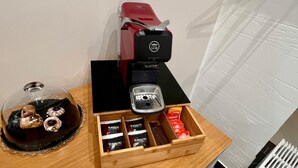 A coffee machine with a tray, a glass container with chocolates, and a wooden box with coffee pods.