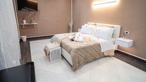 A modern bedroom with a bed, bedside table, TV, and a wall-mounted light.