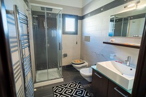 Et moderne badeværelse med en glasbrusekabine, toilet, vask og spejl.