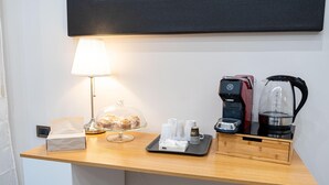 A hotel desk with a lamp, a glass display case with pastries, a coffee maker, and a tray with cups and a box.