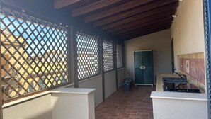 A covered outdoor area with a tiled floor, a metal fence, and a door leading to an interior space.