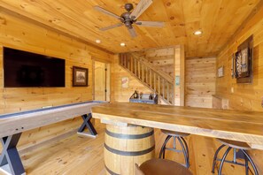 Un intérieur en bois comprenant un espace bar, des murs en bois, un ventilateur de plafond et un escalier.
