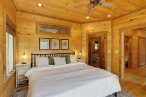 A wooden cabin bedroom with a bed, nightstands, a ceiling fan, and framed pictures on the wall.