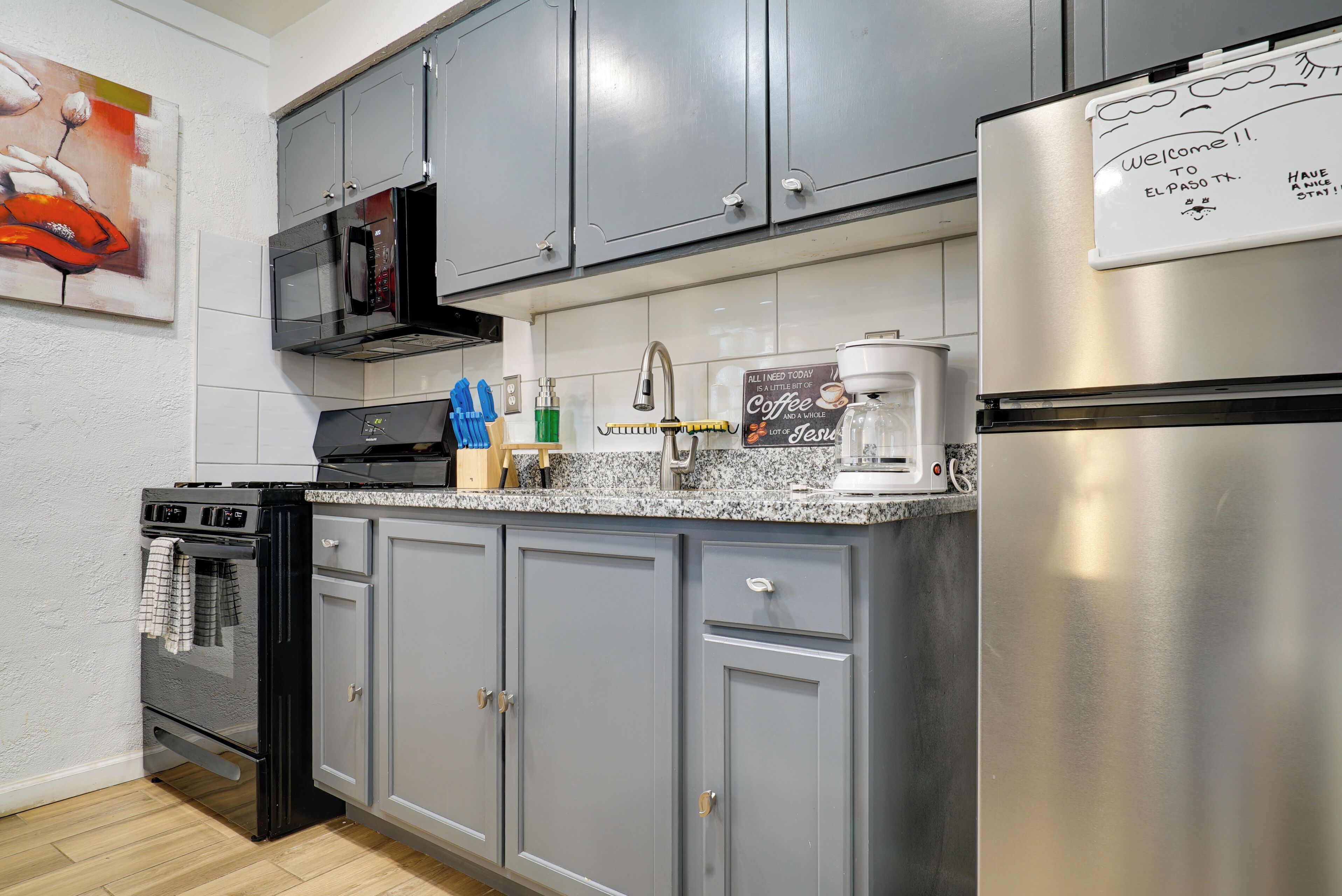 Una cocina moderna con armarios grises, un refrigerador de acero inoxidable, un microondas, una cafetera y una estufa.