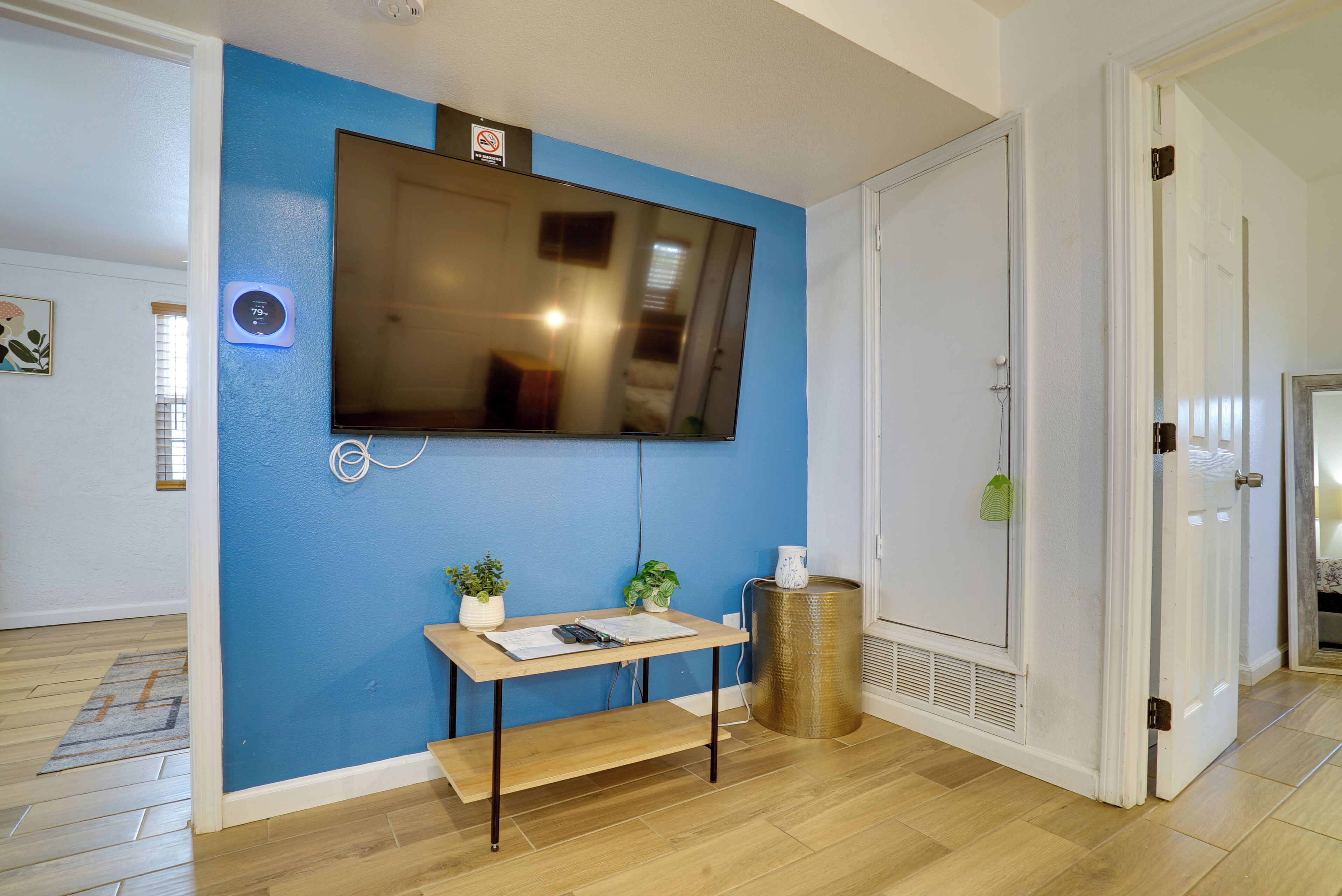 Una habitación con una pared azul de acento, un televisor de pantalla plana montado, una mesa de madera con un banco y un cubo de basura.