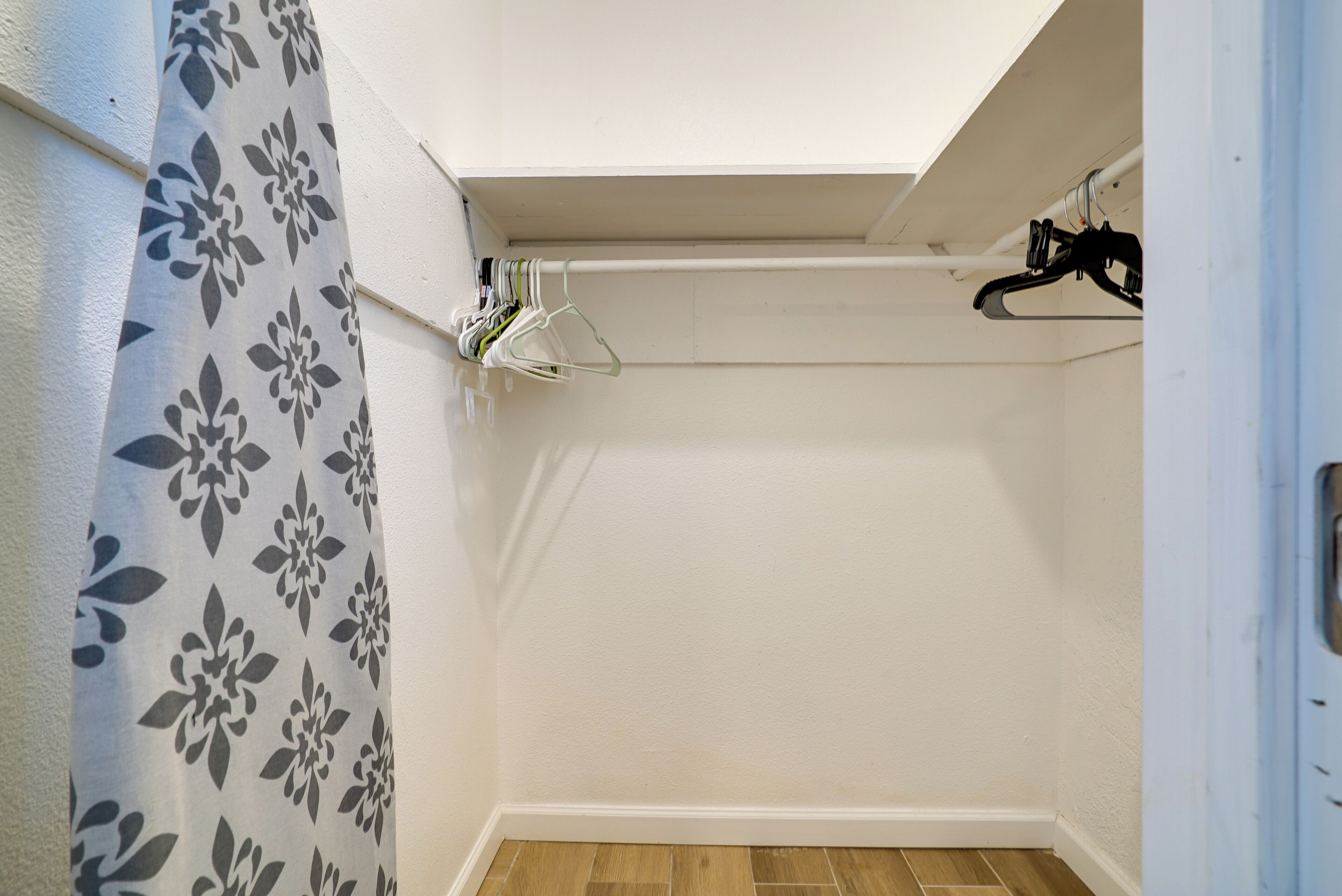 A small, clean bathroom with a shower, a white door, and a blue floral curtain.