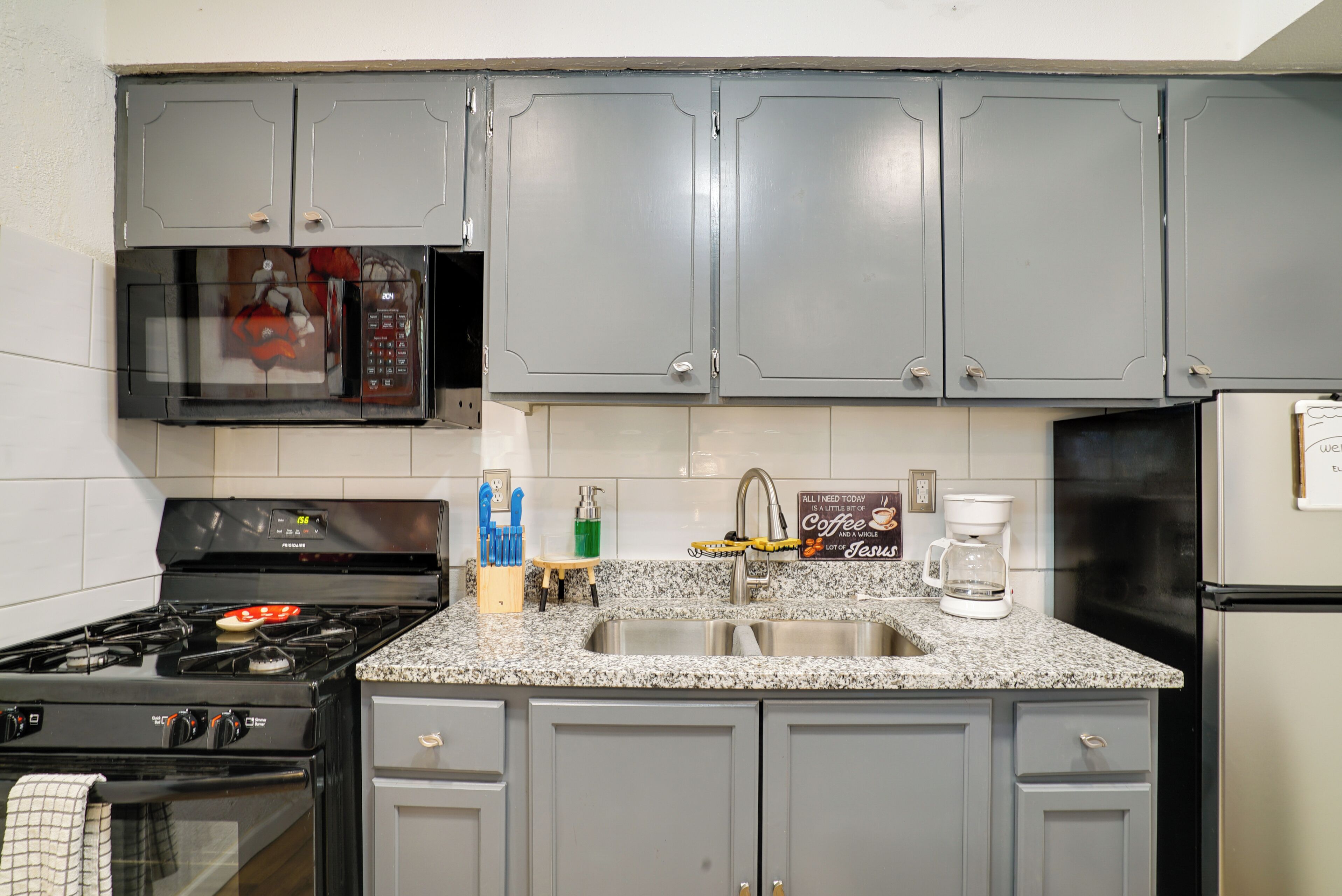 A kitchen with grey cabinets, a stainless steel sink, a stove, and a refrigerator.