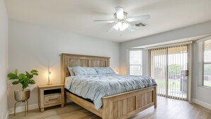 Un dormitorio con una cama de madera, una mesita de noche, una planta en maceta y un ventilador de techo.