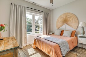 Une chambre avec une grande fenêtre, un lit avec une literie orange, une table de chevet avec une lampe et un élément décoratif mural.