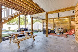 Un patio couvert avec une table et des bancs en bois, un fauteuil suspendu et un barbecue.