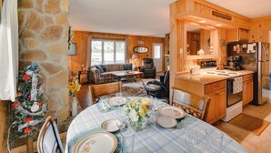 A cozy cabin-style kitchen with a stone wall, wooden cabinets, and a dining area set for a meal. - Lakefront Retreat w/ Pedal Boat & Dock in Kalkaska (Kalkaska)