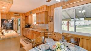 A wooden cabin kitchen with a dining area, wooden cabinets, a refrigerator, and a window overlooking a yard. - Lakefront Retreat w/ Pedal Boat & Dock in Kalkaska (Kalkaska)