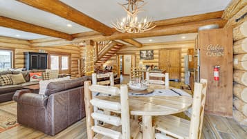 Ein Holzblockhaus-Interieur mit einem Holzessttisch, einer Couch und einer Treppe, die in die obere Etage führt.