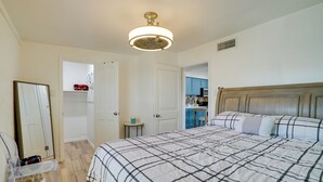 A bedroom with a large bed, a ceiling fan, a mirror, and a door leading to a bathroom.