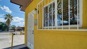 A yellow building with a white door and barred window, a black mat at the entrance, and a clear sky.