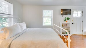 Een slaapkamer met een bed, een aan de muur bevestigde televisie, een deur met raam en een klein plankje met boeken en een plant.