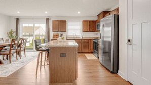 A modern kitchen with wooden cabinets, a stainless steel refrigerator, and a central island. - Lake Erie Retreat – Hidden Village Escape (Perry)