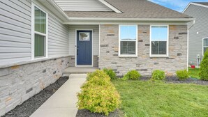 A two-story house with a stone facade, a dark blue front door, and a small front yard with a pathway and bushes. - Lake Erie Retreat – Hidden Village Escape (Perry)