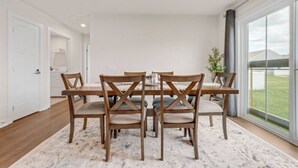 A dining area with a wooden table and chairs, a large window with a view of the outdoors, and a white door leading to another room. - Lake Erie Retreat – Hidden Village Escape (Perry)