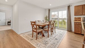 A dining area with a wooden table and chairs, a rug, and a view of the outdoors through large windows. - Lake Erie Retreat – Hidden Village Escape (Perry)