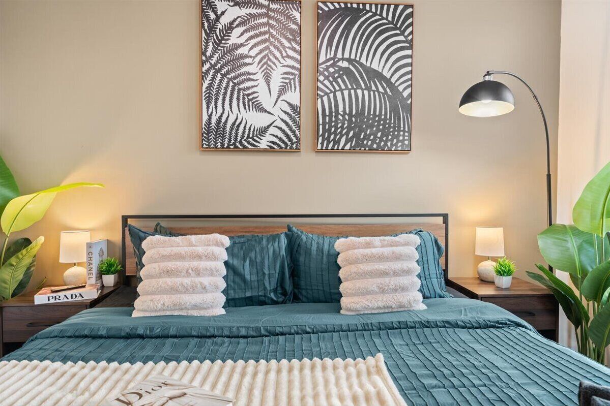 A neatly arranged bedroom with a bed, pillows, bedside tables, and wall art.