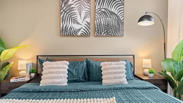 A neatly arranged bedroom with a bed, pillows, bedside tables, and wall art.