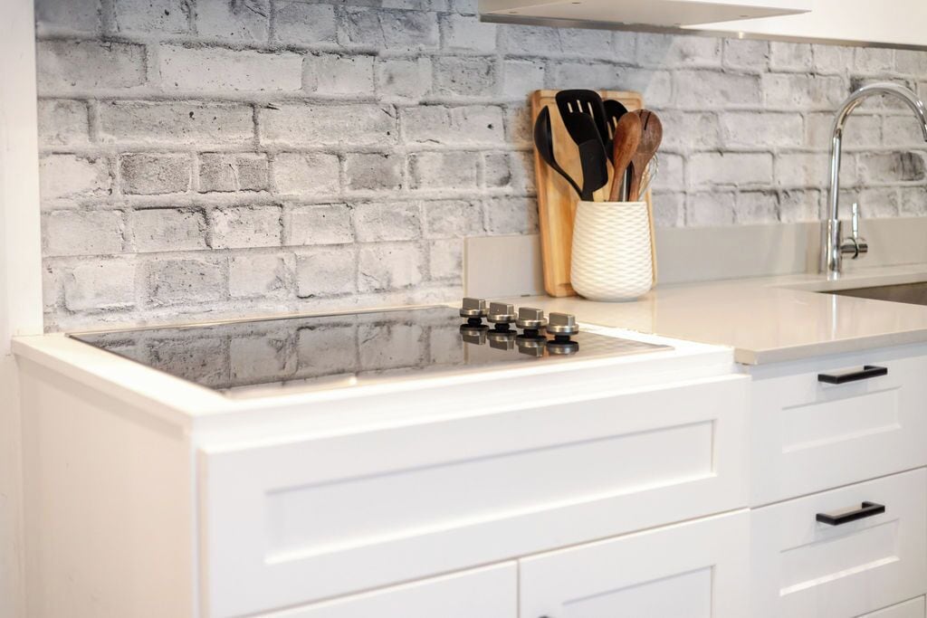 Una cocina con encimera blanca, pared de ladrillo y un portal utensilios con utensilios de madera.
