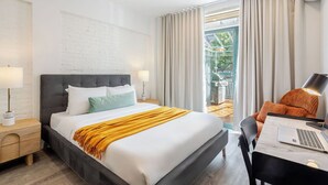 Una moderna camera d'albergo con un letto grande, una scrivania con un portatile e vista su un giardino dalla finestra.
