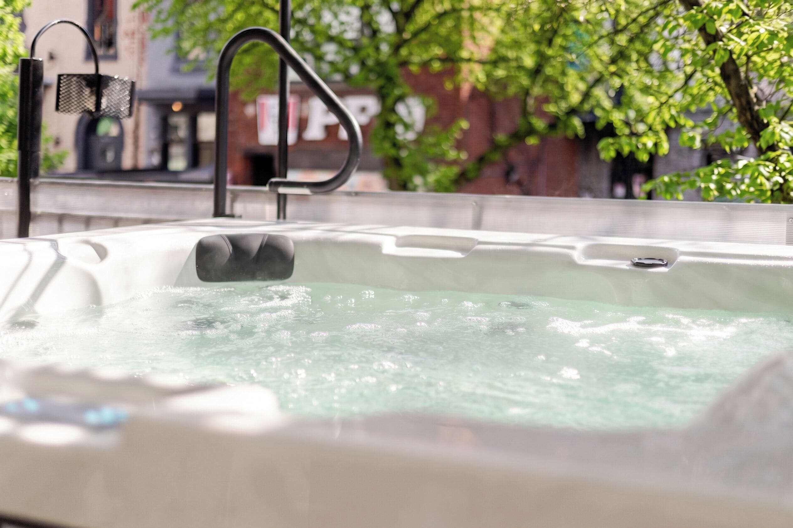 A hot tub with a metal faucet and a mesh cover, surrounded by greenery and a building in the background.