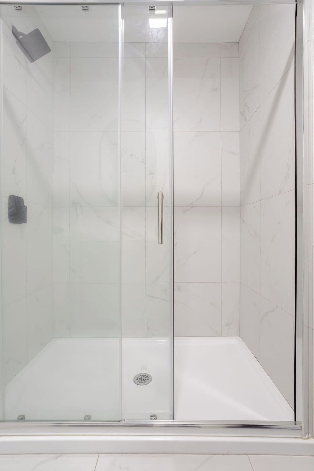 A glass-enclosed shower stall with a marble-tiled wall and floor, a handheld showerhead, and a control panel.