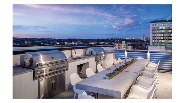 An outdoor patio with a grill, seating, and a view of a cityscape at dusk. - Chic Studio Deluxe Hotel Suite in the Heart of Austin (Austin)
