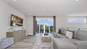A modern living room with a grey sofa, a coffee table, and a TV on the wall. - Inviting Condo w/ Pool Table near Disney, Resort & Waterpark Access - B34-246 (Kissimmee)