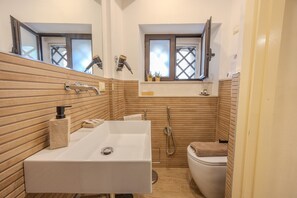 A bathroom with a large white sink, a toilet, and a shower. There are wooden panel walls and a window above the toilet. - Damas Home, apartment in St. Onofrio Square (Palermo)