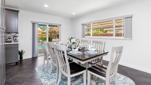 A dining area with a table set for six, white chairs, and a view of a backyard through a glass door.