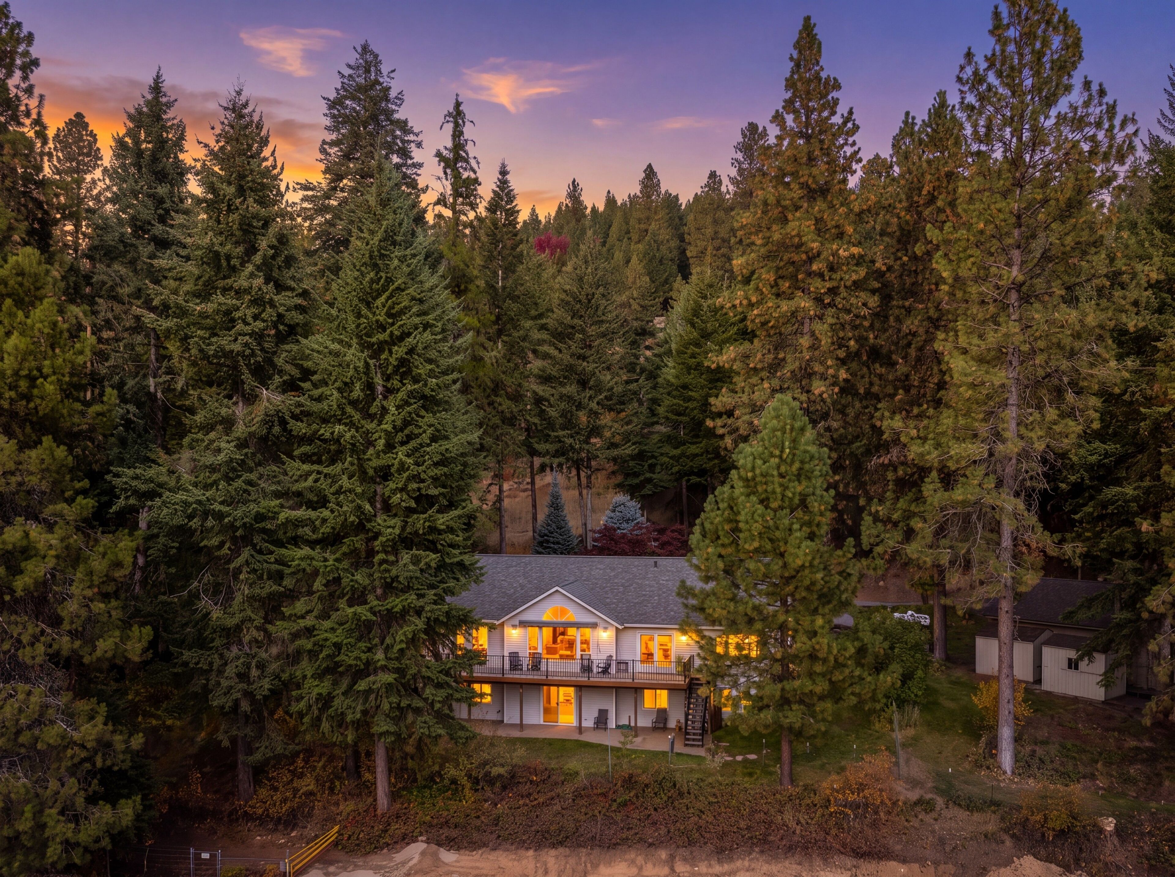 A two-story house surrounded by dense forest, with a visible deck and a large window on the second floor.