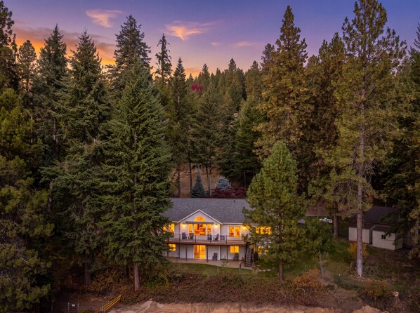 A two-story house surrounded by dense forest, with a visible deck and a large window on the second floor.
