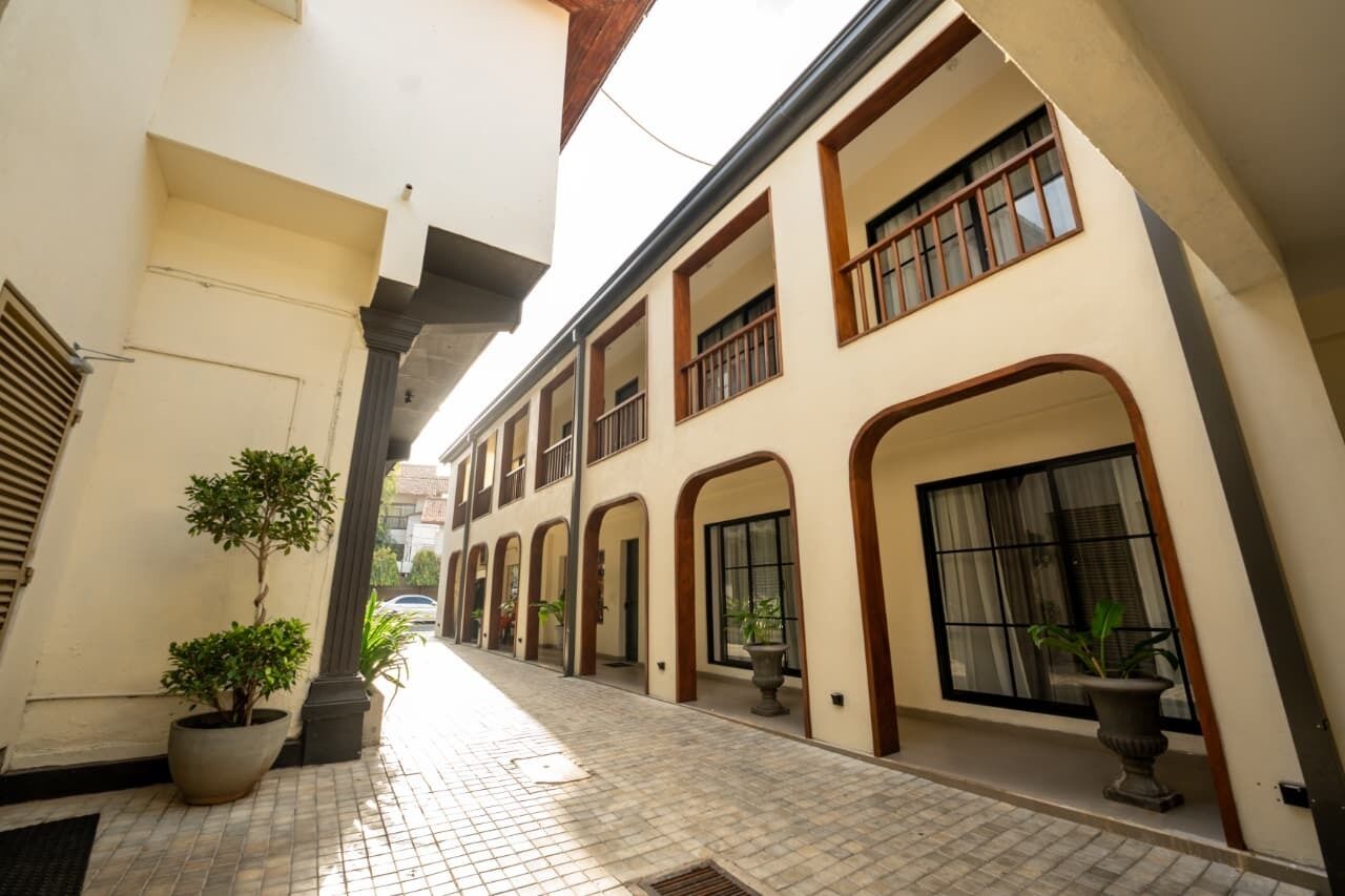 A narrow corridor with tiled flooring, potted plants, and a building with multiple windows and arches.