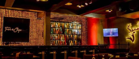 A bar area with a neon sign, a television screen, and a wall with a deer logo.