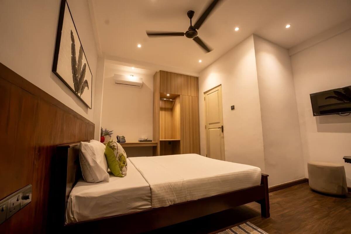 A bedroom with a bed, a ceiling fan, a mounted TV, and a wooden wardrobe.