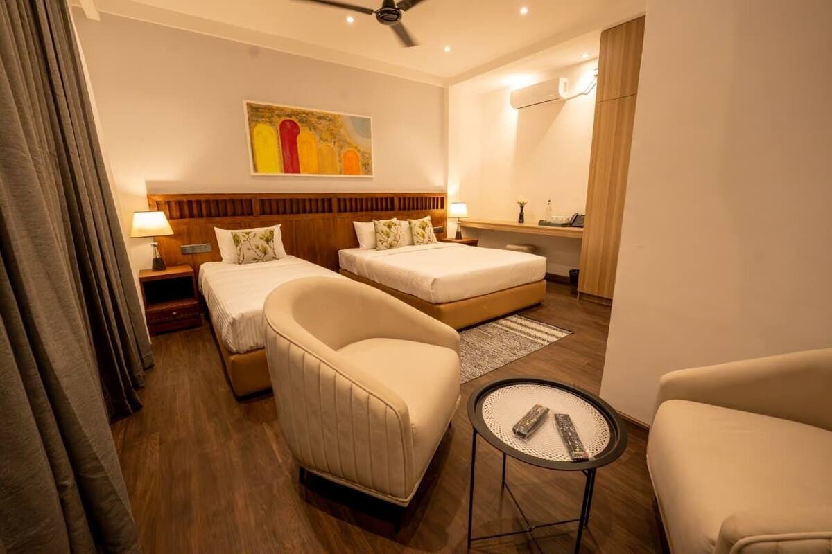 A hotel room with two beds, a sofa, a small table, and a ceiling fan.