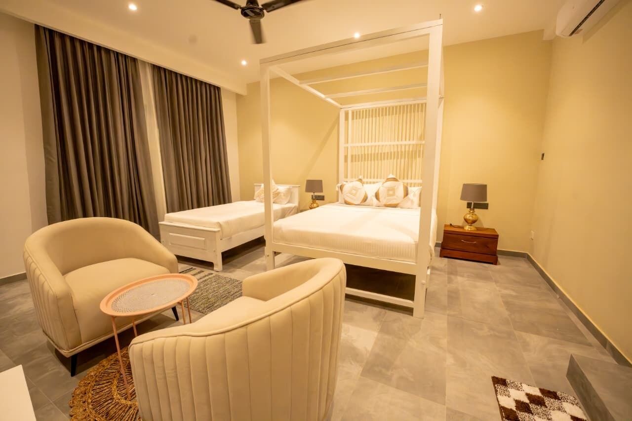 A modern bedroom with a four-poster bed, two bedside tables, a chair, and a small round table.