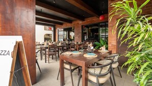 Un restaurant avec des tables et des chaises en bois, des murs en briques et une grande plante en pot.