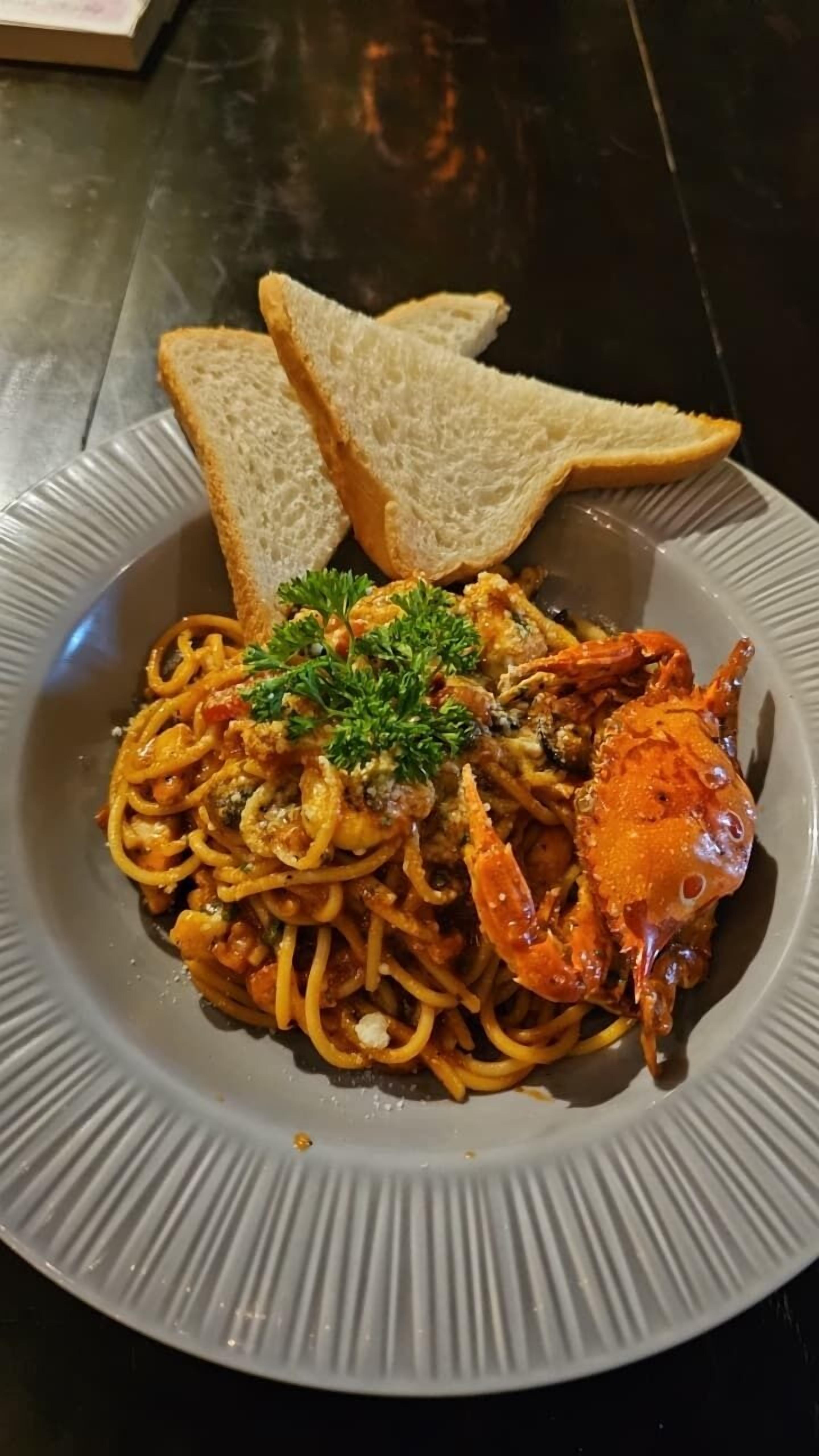 A plate of spaghetti with a crab, garnished with parsley, and two slices of bread on a dark table.